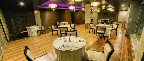A restaurant with round tables, chairs, and a wooden floor.