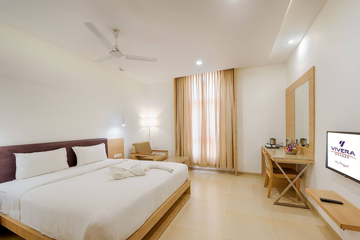 A hotel room with a bed, desk, chair, and a TV on the wall.
