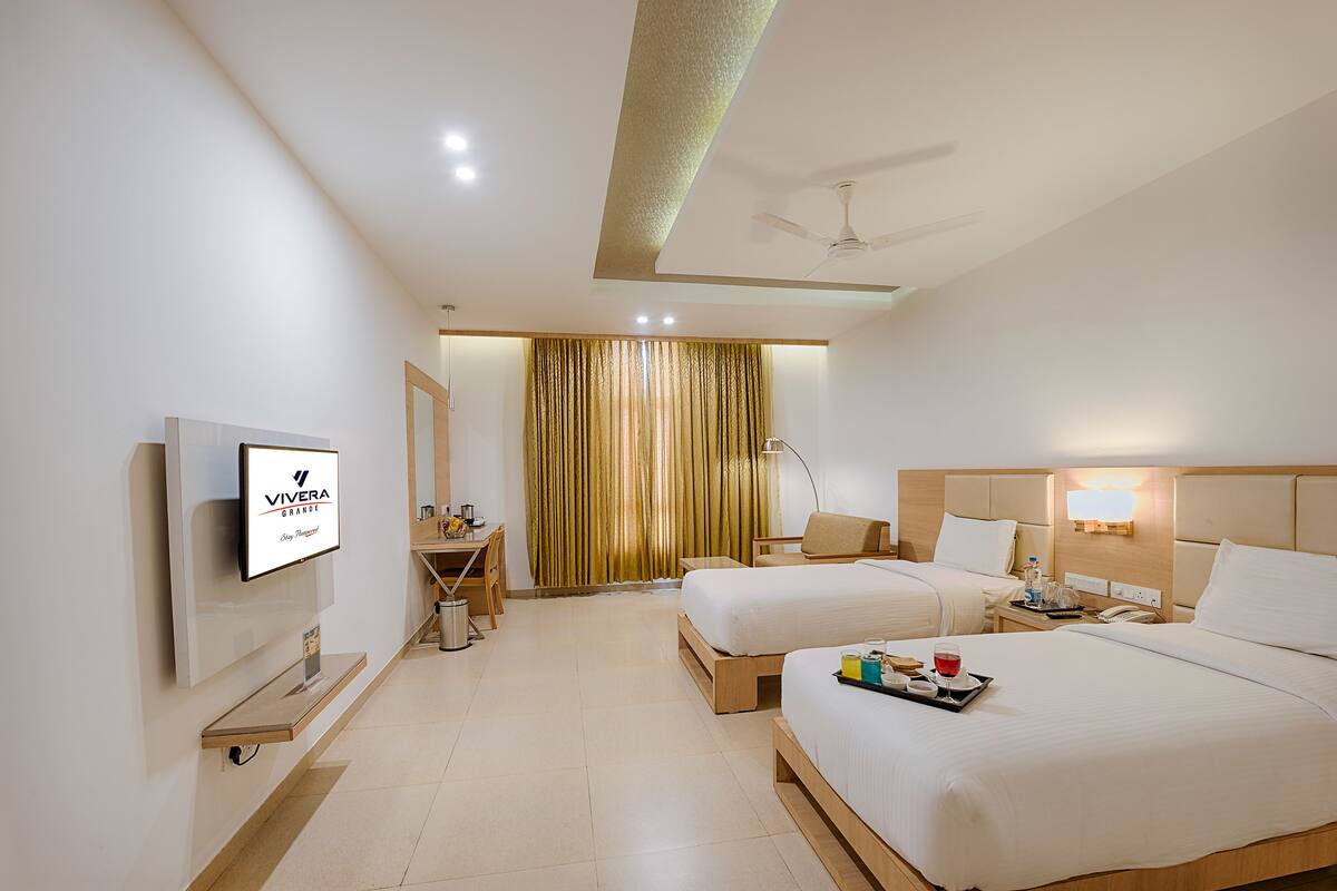 A hotel room with two beds, a desk, a TV, and a bathroom.