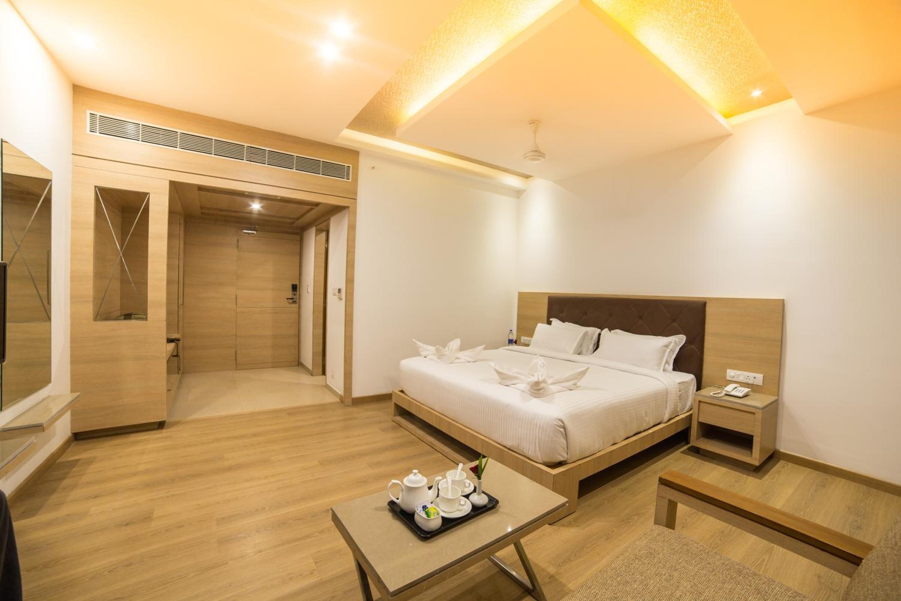 Een moderne hotelkamer met een houten vloer, een bed met witte lakens, een nachtkastje met een telefoon en een klein tafeltje met een dienblad met ontbijtartikelen.