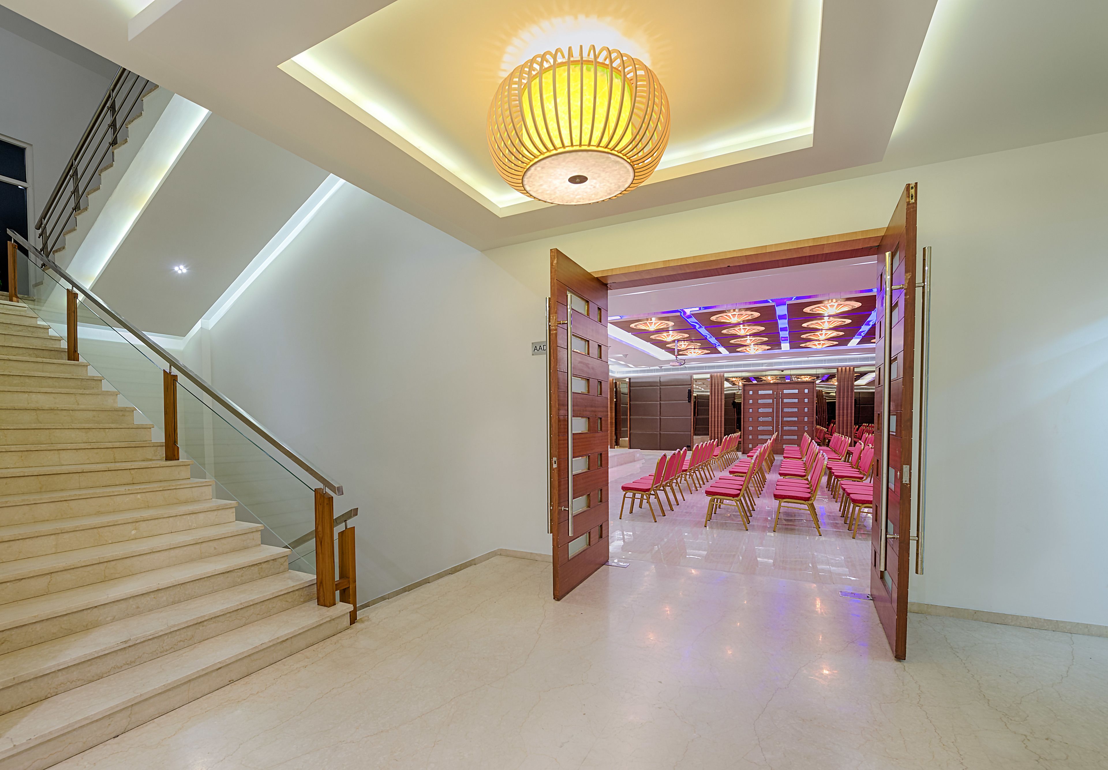 Eine Hotellobby mit Treppe, einer Kristallleuchtre und Reihen von rosa Stühlen.