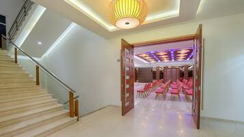 Eine Hotellobby mit Treppe, einer Kristallleuchtre und Reihen von rosa Stühlen.
