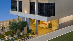 A modern hotel with a geometric facade, illuminated signage, and a landscaped outdoor area with pathways and greenery. - Vivera Grande (Thindukkal)