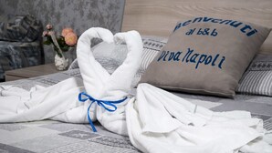 A neatly made bed with a towel heart, a pillow with 'Benvenuti al b&b Viva Napoli' text, and a vase with flowers on a nightstand. - B&B Viva Napoli (Naples)