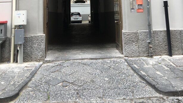 A building entrance with a large arched doorway, a vehicle parked inside, and a stone-paved entrance area. - B&B Viva Napoli (Naples)