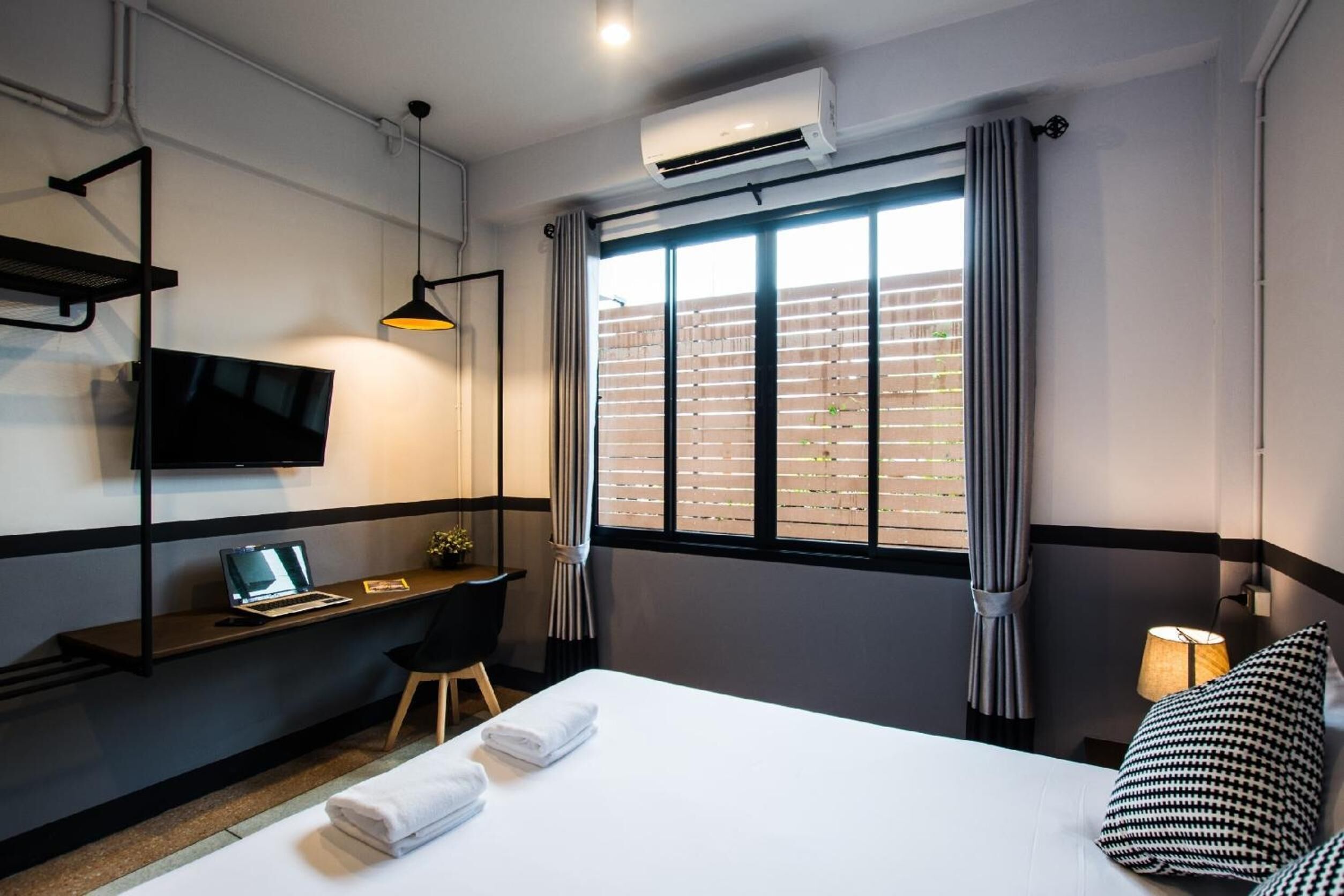 A hotel room with a bed, a desk with a laptop, a TV, and a window with curtains.