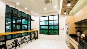 A modern kitchen with a wooden countertop, black stools, and a large window offering a view of greenery. - BY Hotel Kanchanaburi (Kanchanaburi)