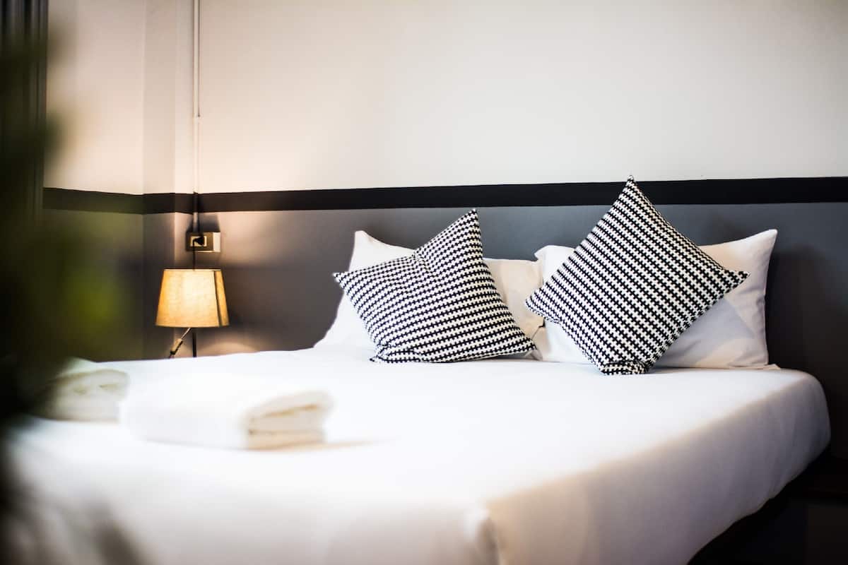 A neatly made bed with white linens and two black and white patterned pillows.