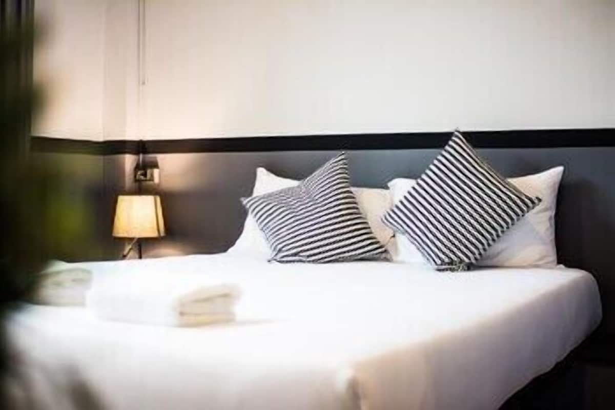 A neatly made bed with striped pillows, a bedside lamp, and a dark headboard.