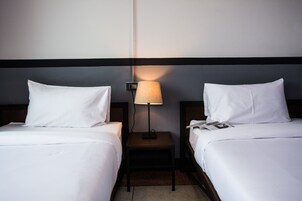 Habitación de hotel con dos camas, una mesita de noche con lámpara y un teléfono de pared.