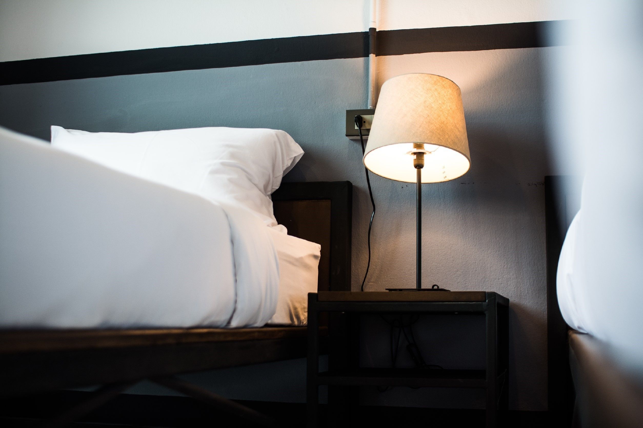 A neatly made bed with white linens, a bedside lamp, and a wooden nightstand.