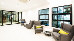 A modern interior with grey armchairs, a round coffee table, and large windows offering views of the outside. - BY Hotel Kanchanaburi (Kanchanaburi)