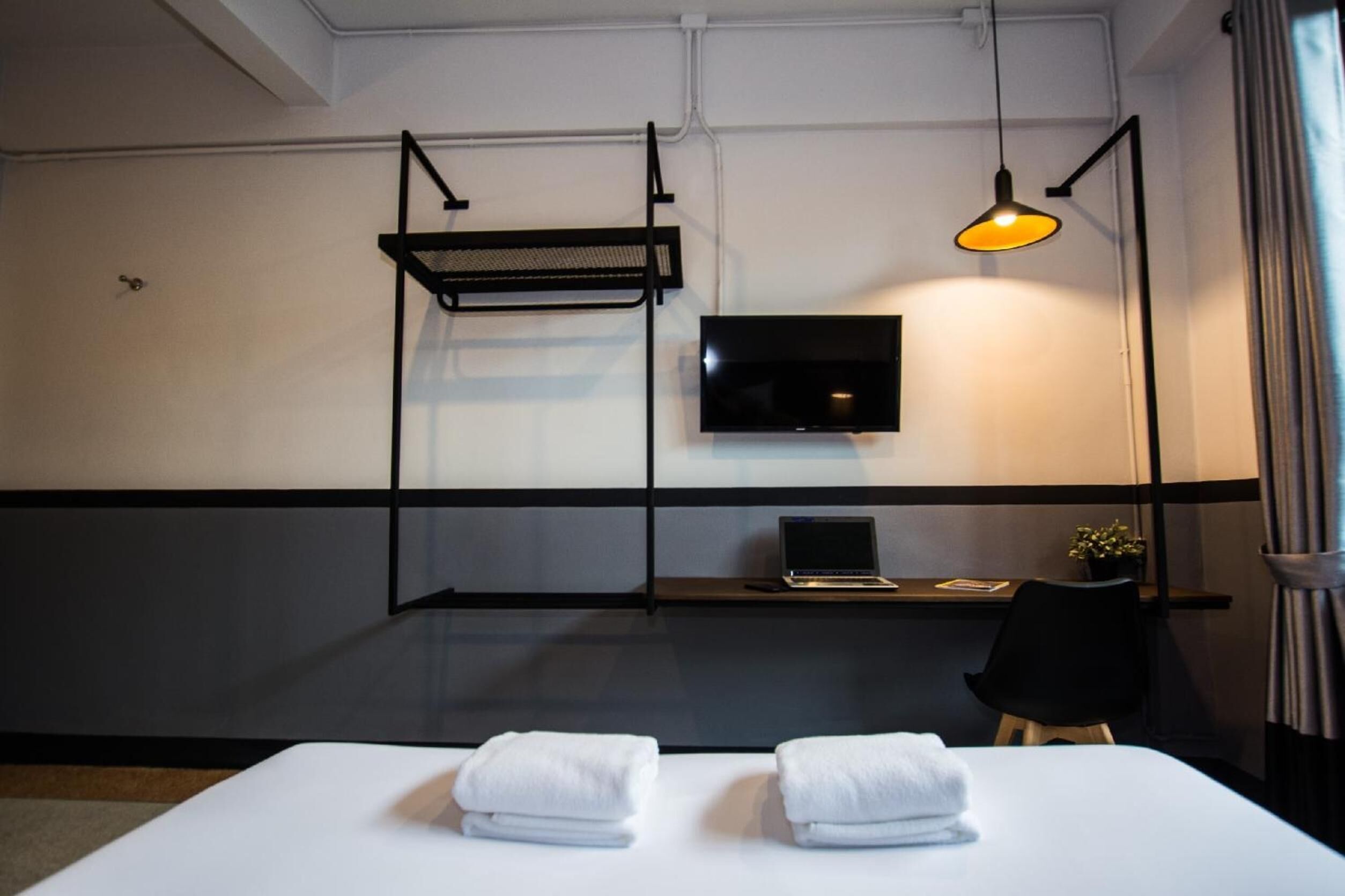 A hotel room with a bed, a desk with a laptop, a TV, and a hanging light fixture.