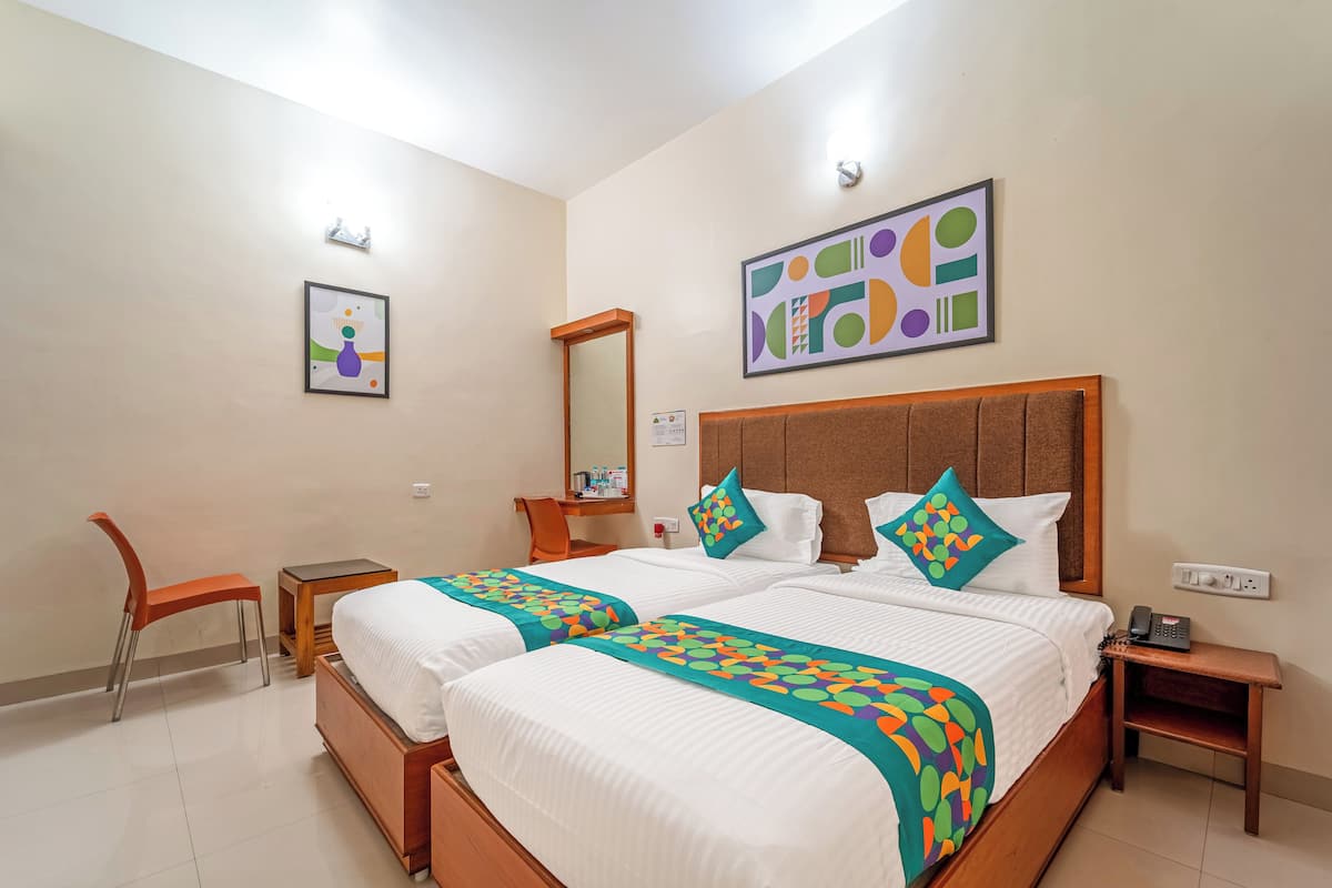 A hotel room with two beds, a desk, a chair, a mirror, and artwork on the walls.