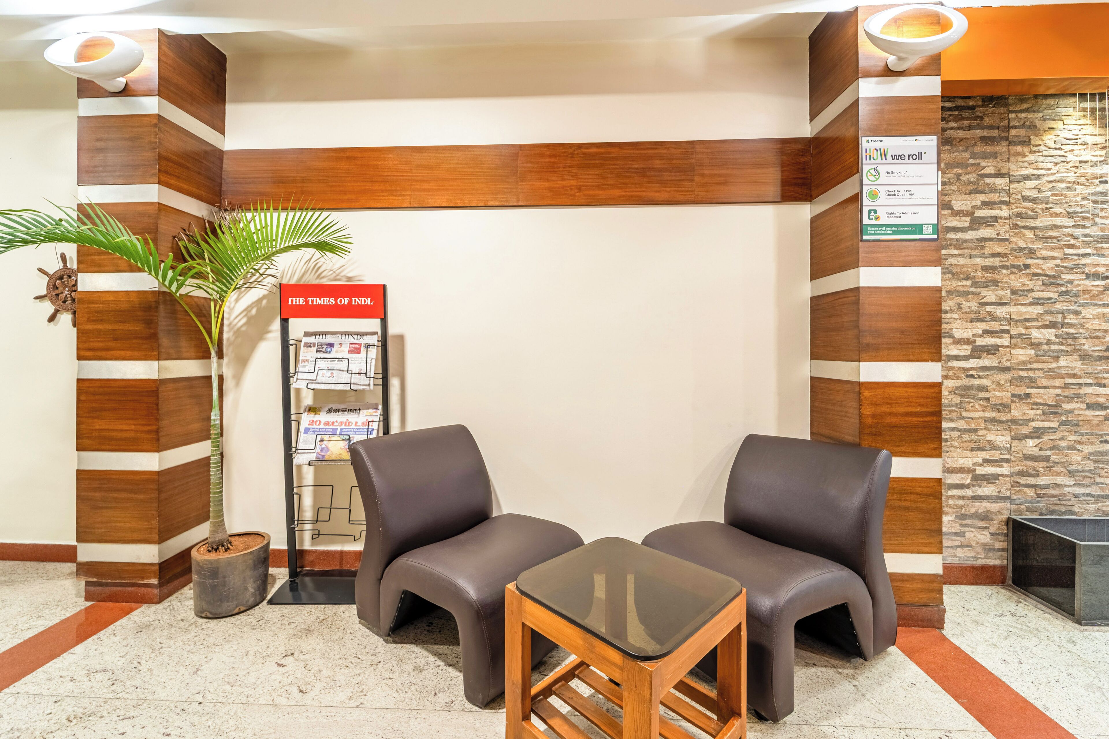 A reception area with a reception desk, two leather chairs, a small table, a potted plant, a magazine rack, and a stone wall.