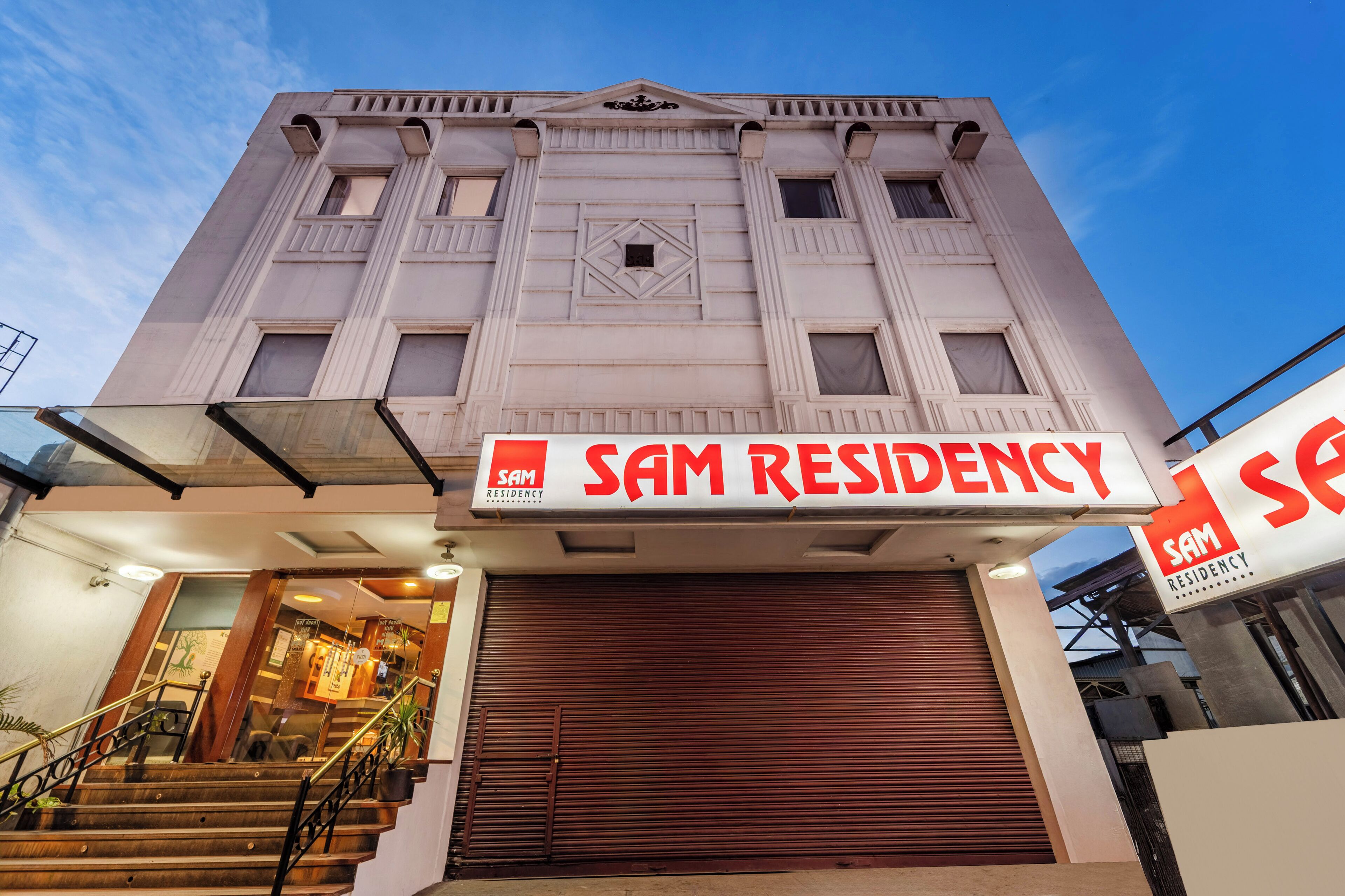 A building with a sign reading "SAM RESIDENCY" and a closed shutter door.