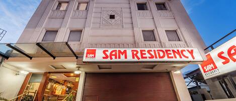 A building with a sign reading "SAM RESIDENCY" and a closed shutter door.