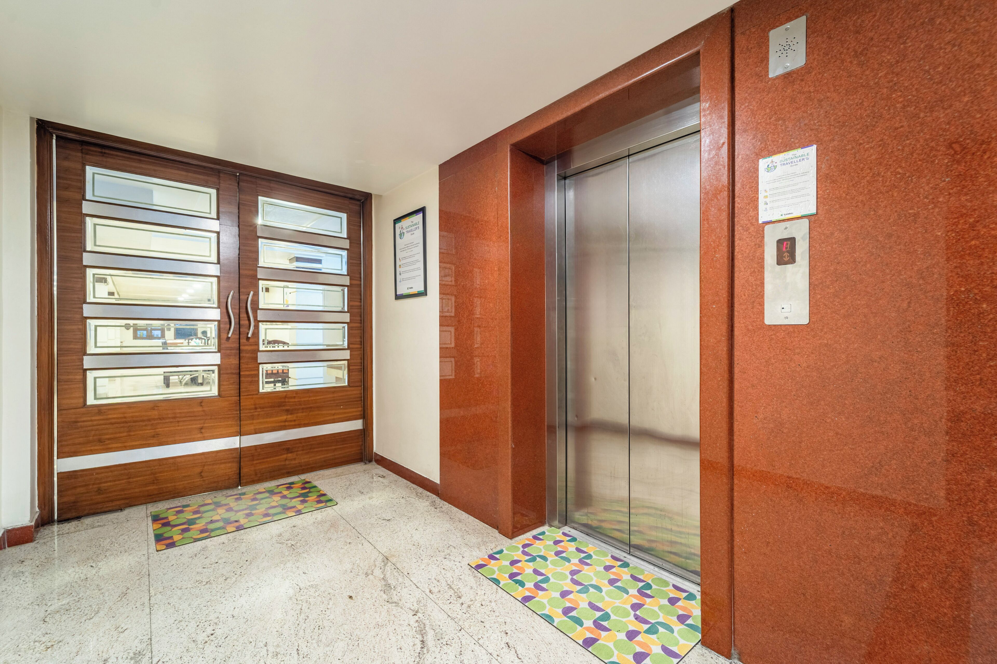 A hallway with a wooden door with glass panels, a metal elevator, and a patterned rug on the floor.