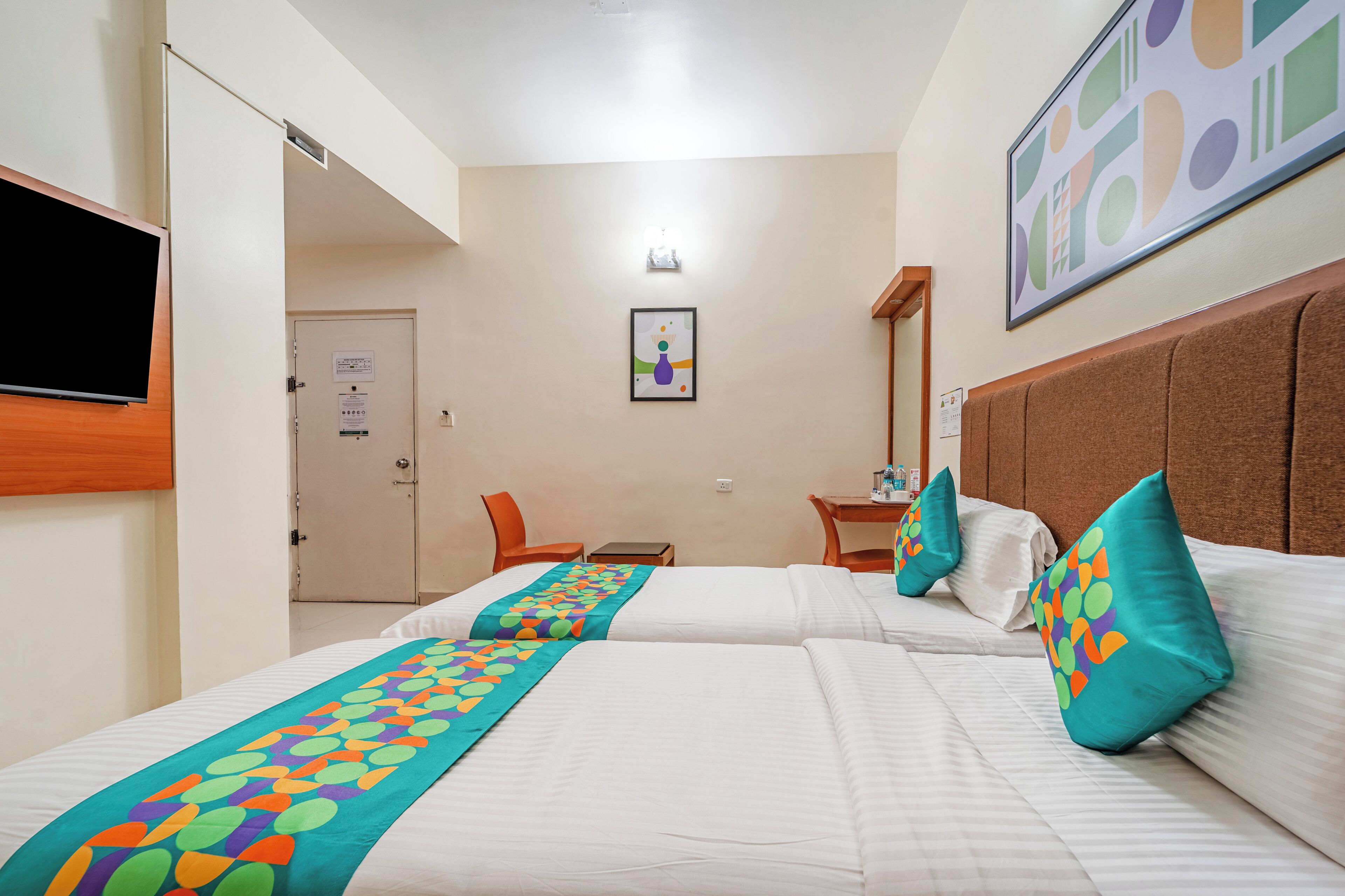 A hotel room with two beds, a TV mounted on the wall, a desk, and a chair.