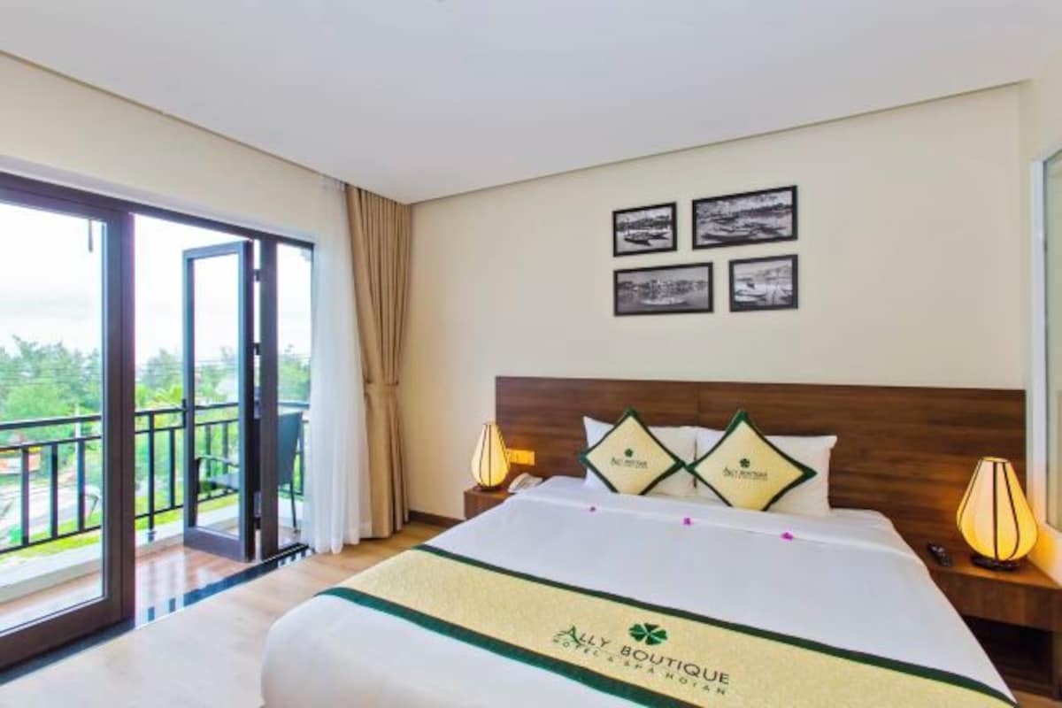 A hotel room with a large bed, a balcony with a view, and artwork on the wall.