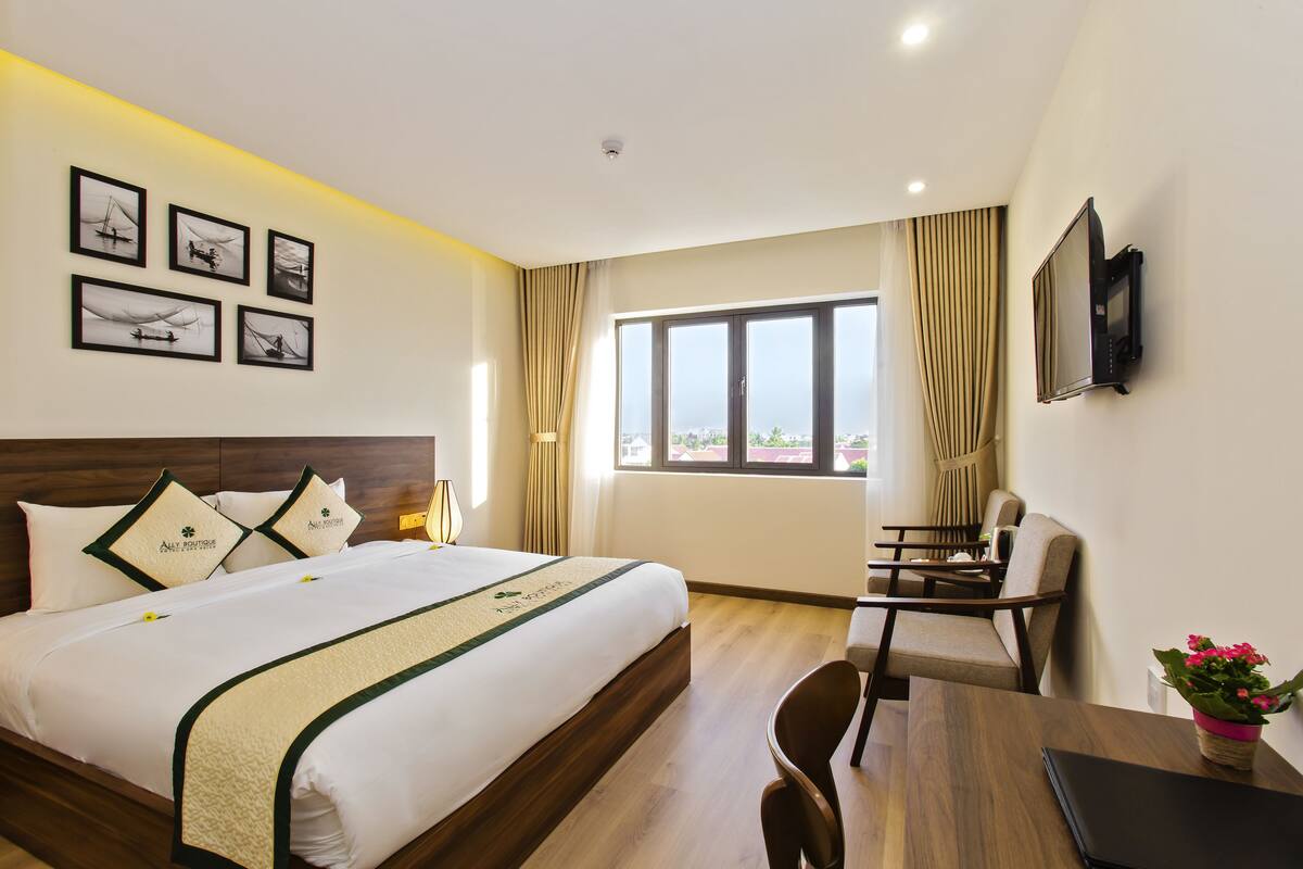 Ein Hotelzimmer mit einem großen Bett, einem Schreibtisch, einem Sessel, einem Fernseher und einem Fenster mit Vorhängen.