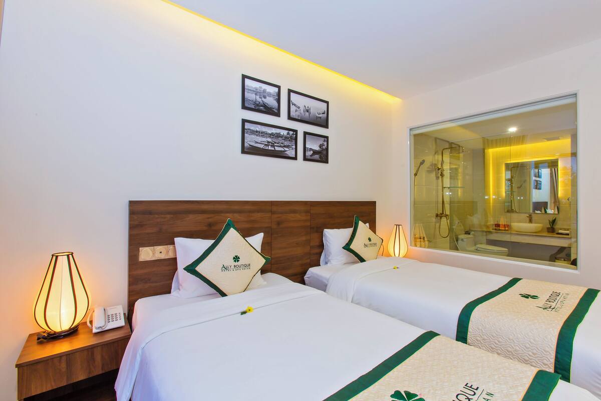 Ein Hotelzimmer mit zwei Betten, einem hölzernen Kopfteil, einem Nachttisch mit Lampe, einem Telefon und einem Wandbild.