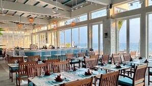 A restaurant with a view of the sea, wooden chairs, tables, ceiling fans, and hanging lights. - Ally Beach Boutique Hotel Hoian (Da Nang)