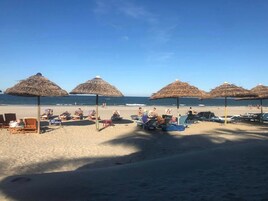 Una playa con sombrillas de paja y sillas de descanso.