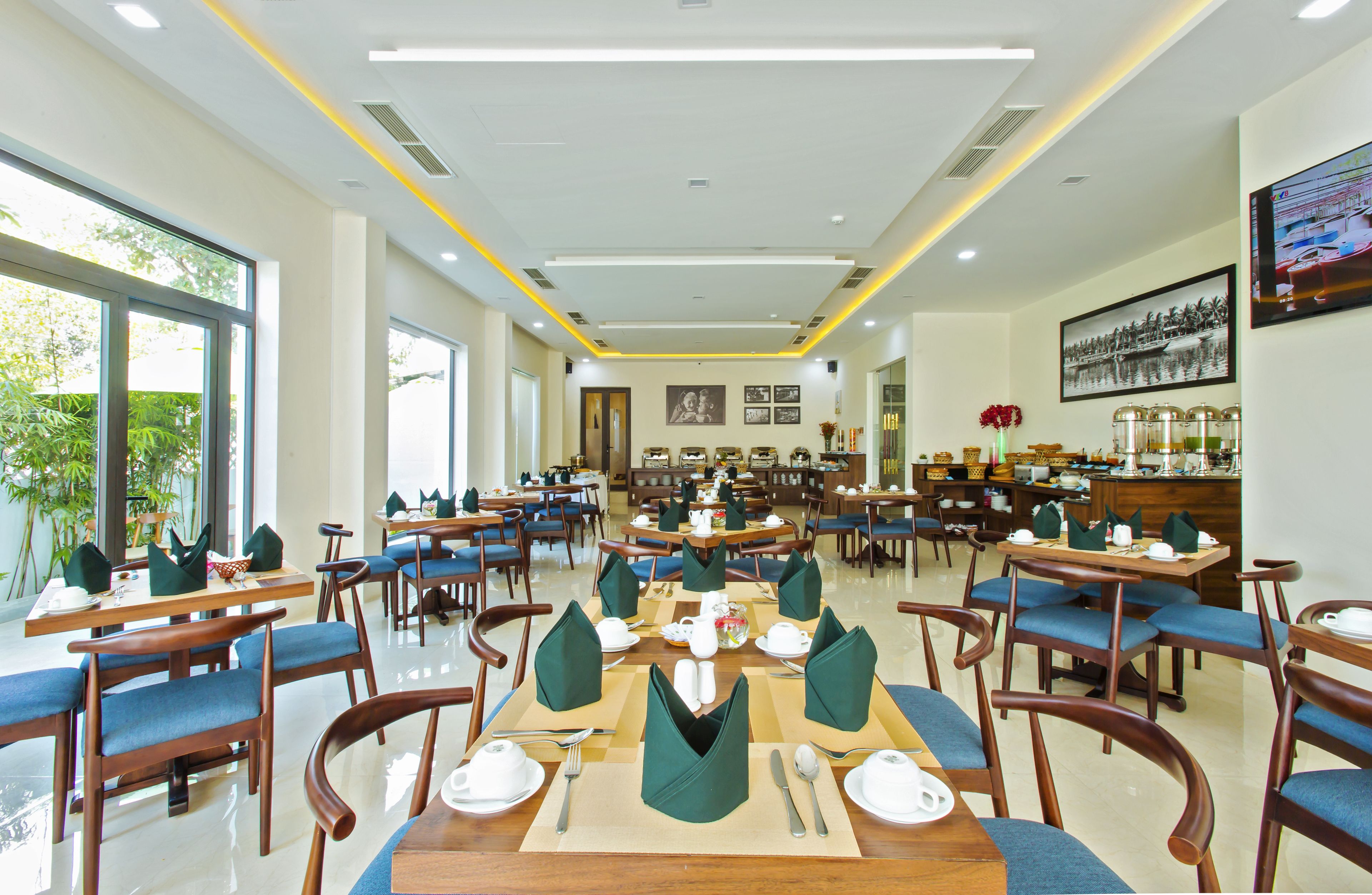 A spacious dining area with multiple tables and chairs, large windows, and a modern ceiling design.