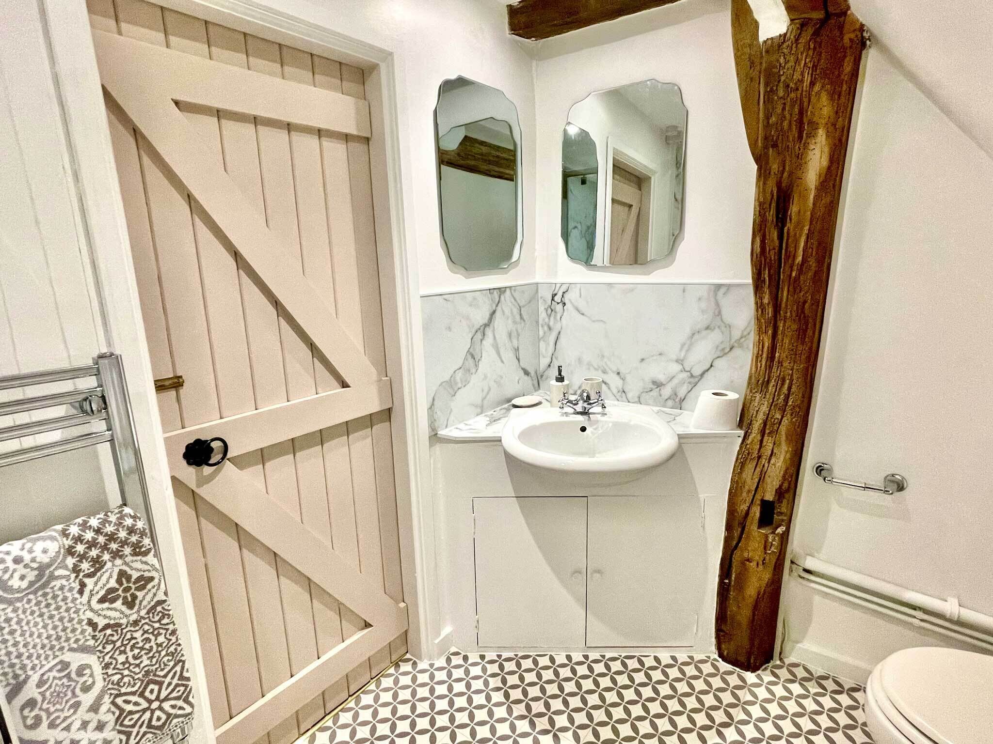 A bathroom with a white sink, two mirrors, a patterned floor, and a wooden door.