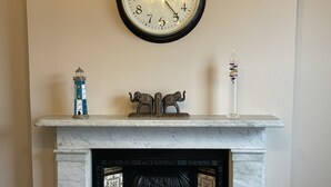 Una chimenea con un reloj encima, una mesa con un plato y una taza, y un adorno en la repisa.