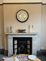 A fireplace with a clock above it, a table with a plate and a cup, and a decorative item on the mantel.