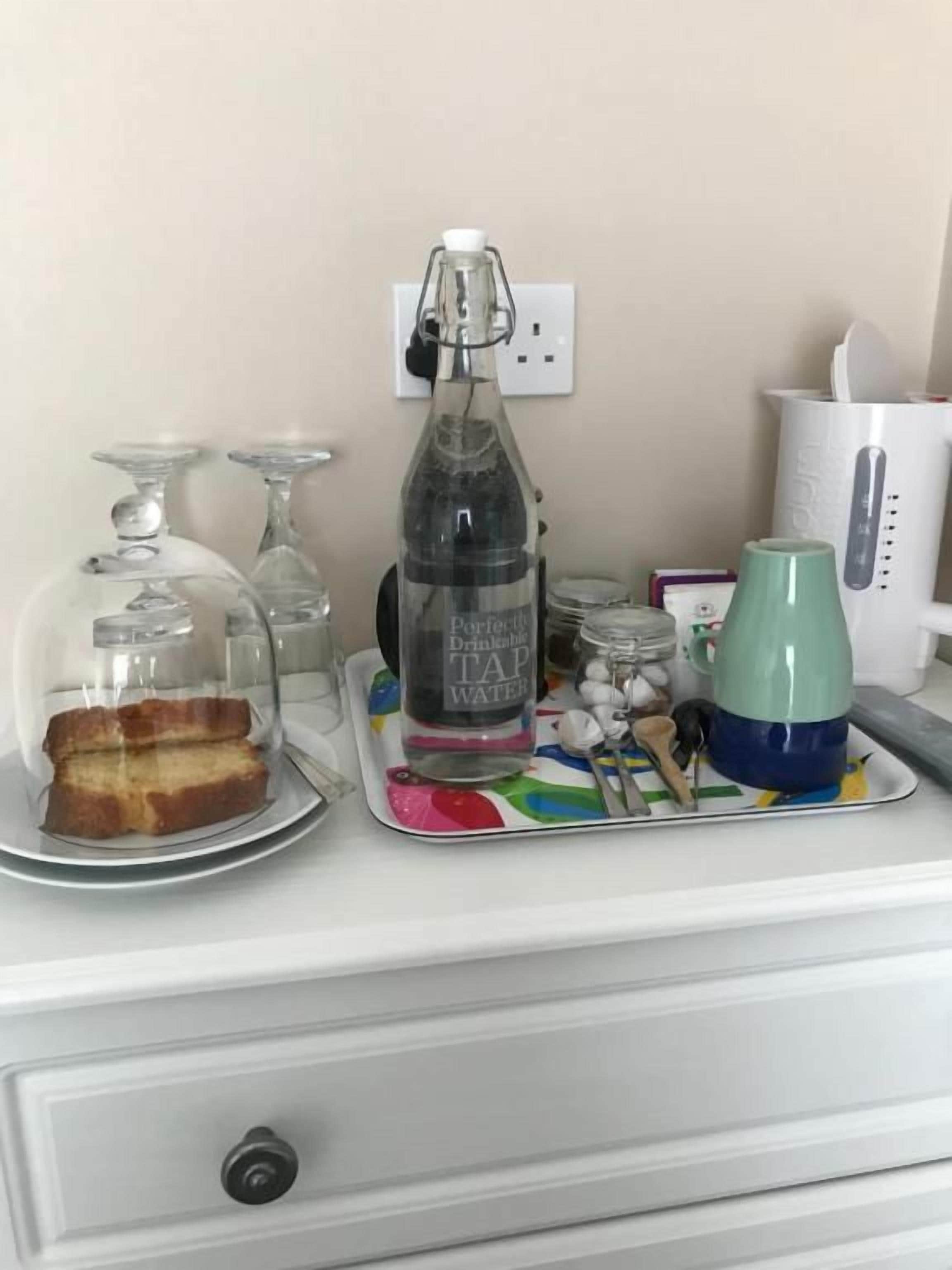 A kitchen counter with a bottle of water, a glass jar, a green mug, and a plate with bread.