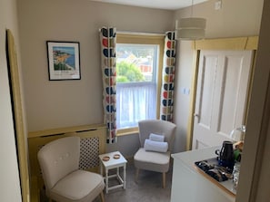 Una habitación pequeña y acogedora con ventana, una silla, una mesita y una zona de kitchenette.