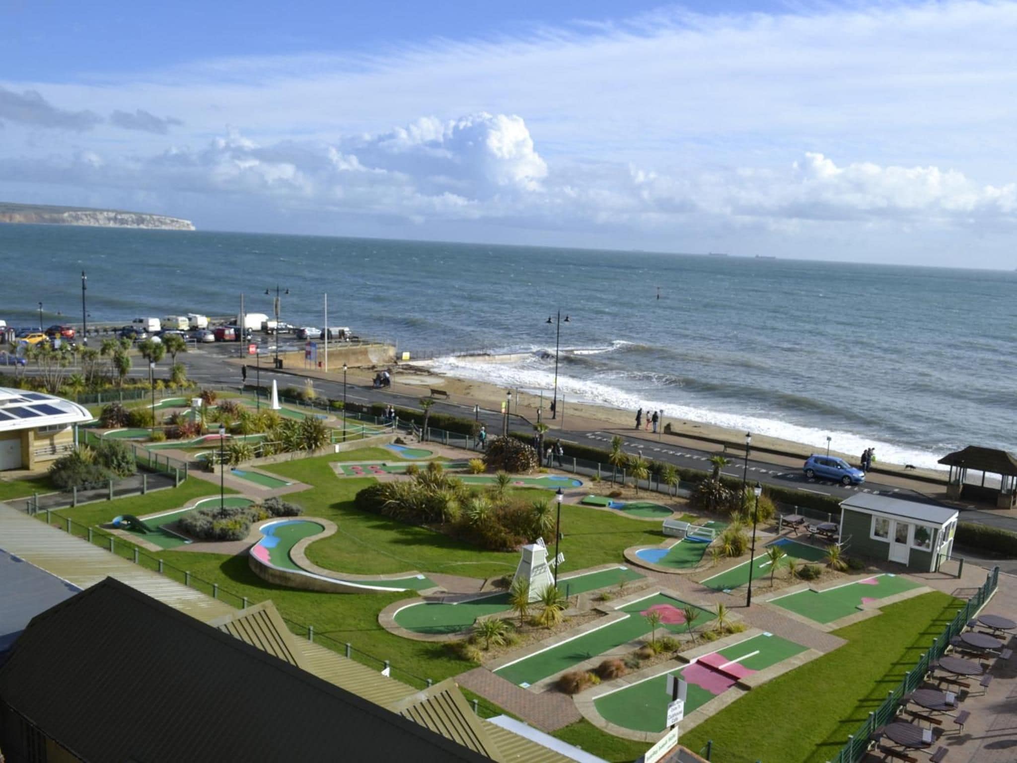A coastal view with a road leading to a beach, a parking area, and a golf course.