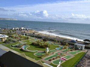 Vista costera con una carretera que lleva a una playa, un estacionamiento y un campo de golf.