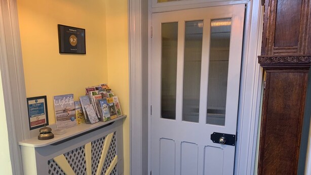 Un pasillo con una puerta blanca, un tablón de anuncios con varios objetos y una pequeña consola con revistas.