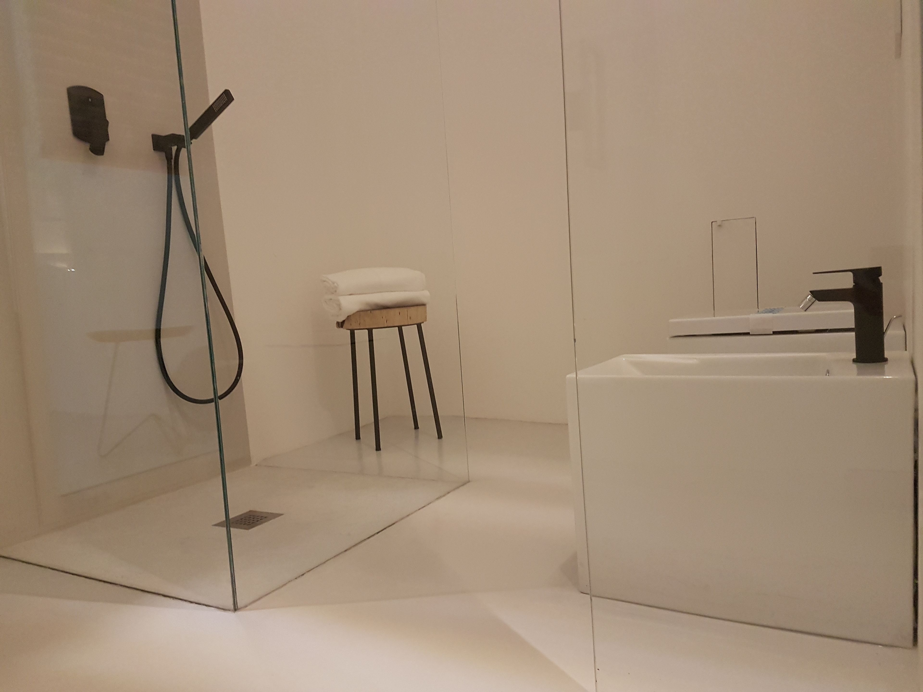 Ein modernes Badezimmer mit Duschkabine aus Glas, einem Holzschemel und einem weißen Waschbecken.