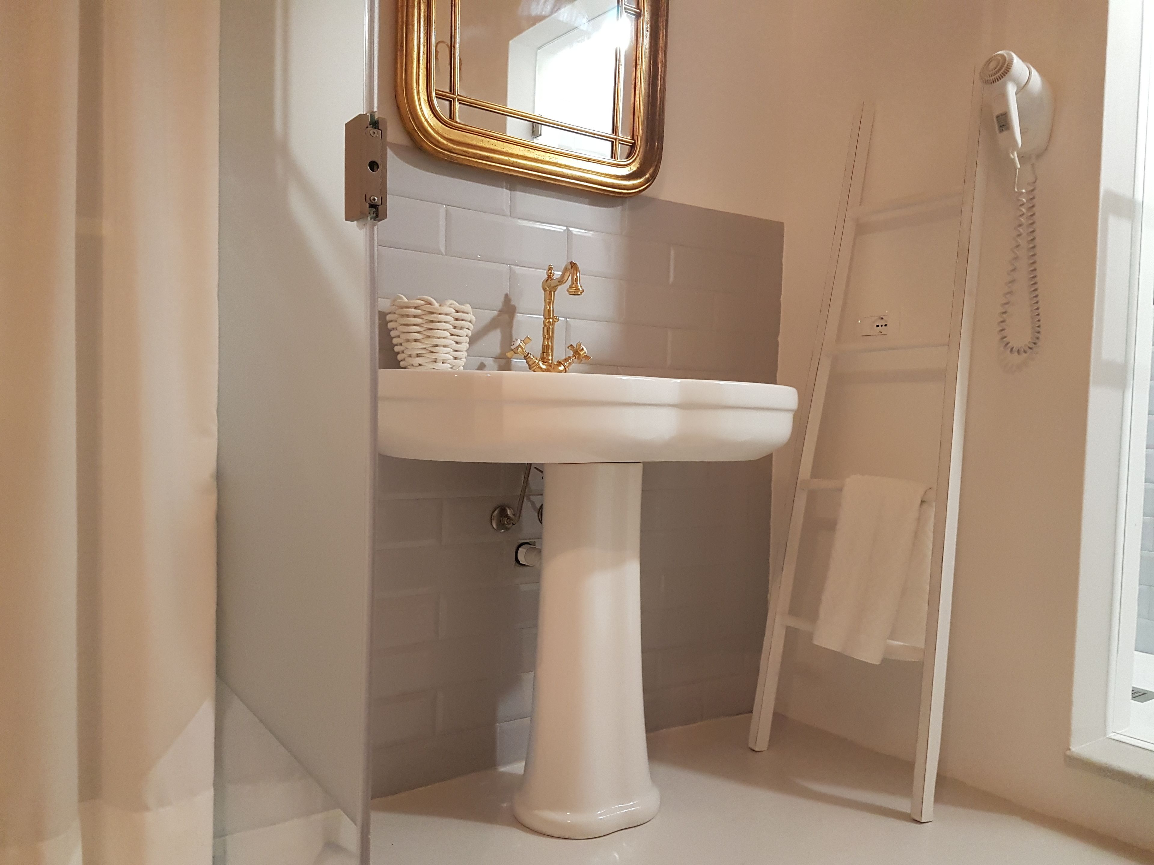 A bathroom with a white pedestal sink, a gold-framed mirror, and a white towel rack.