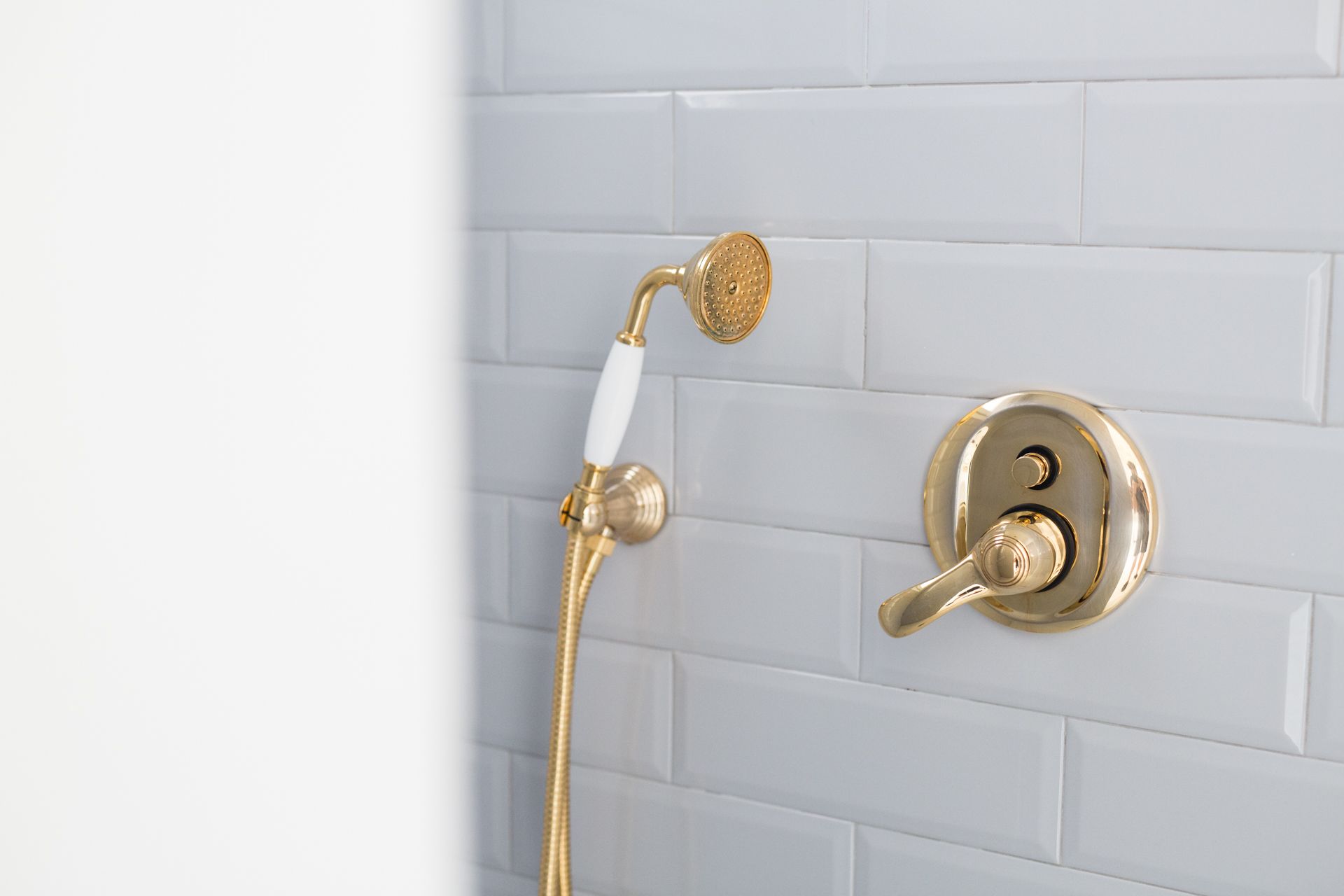 Ein Badezimmer mit Duschkopf und Wasserhahn in Gold, vor einer weißen Fliesenwand.