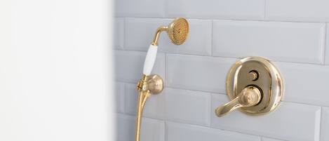 Une salle de bain avec une pomme de douche et un robinet dorés, le tout mis en valeur par un mur recouvert de carreaux blancs.