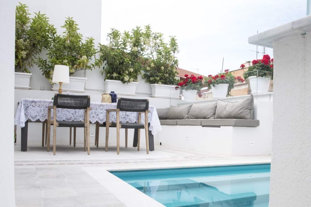 Una zona junto a la piscina con una mesa, sillas, un sofá y plantas en macetas.