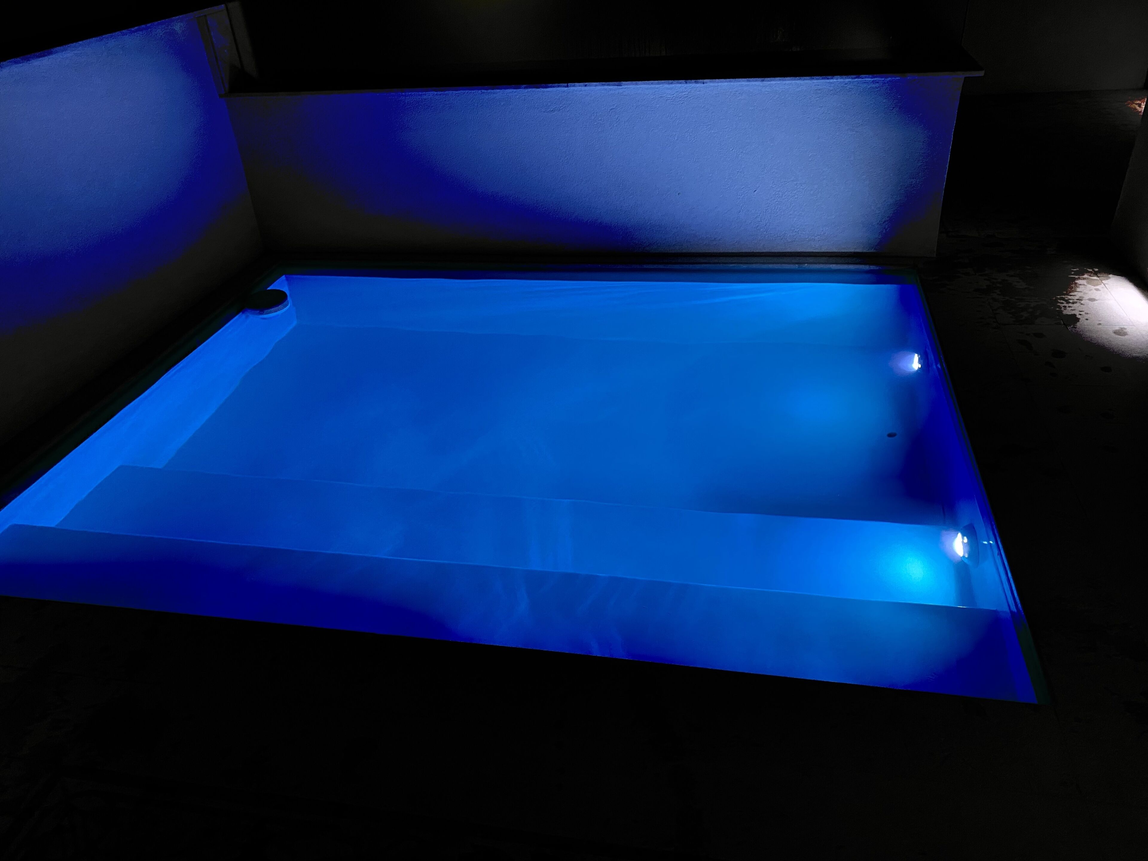 Quarto com piscina retangular iluminada em azul.