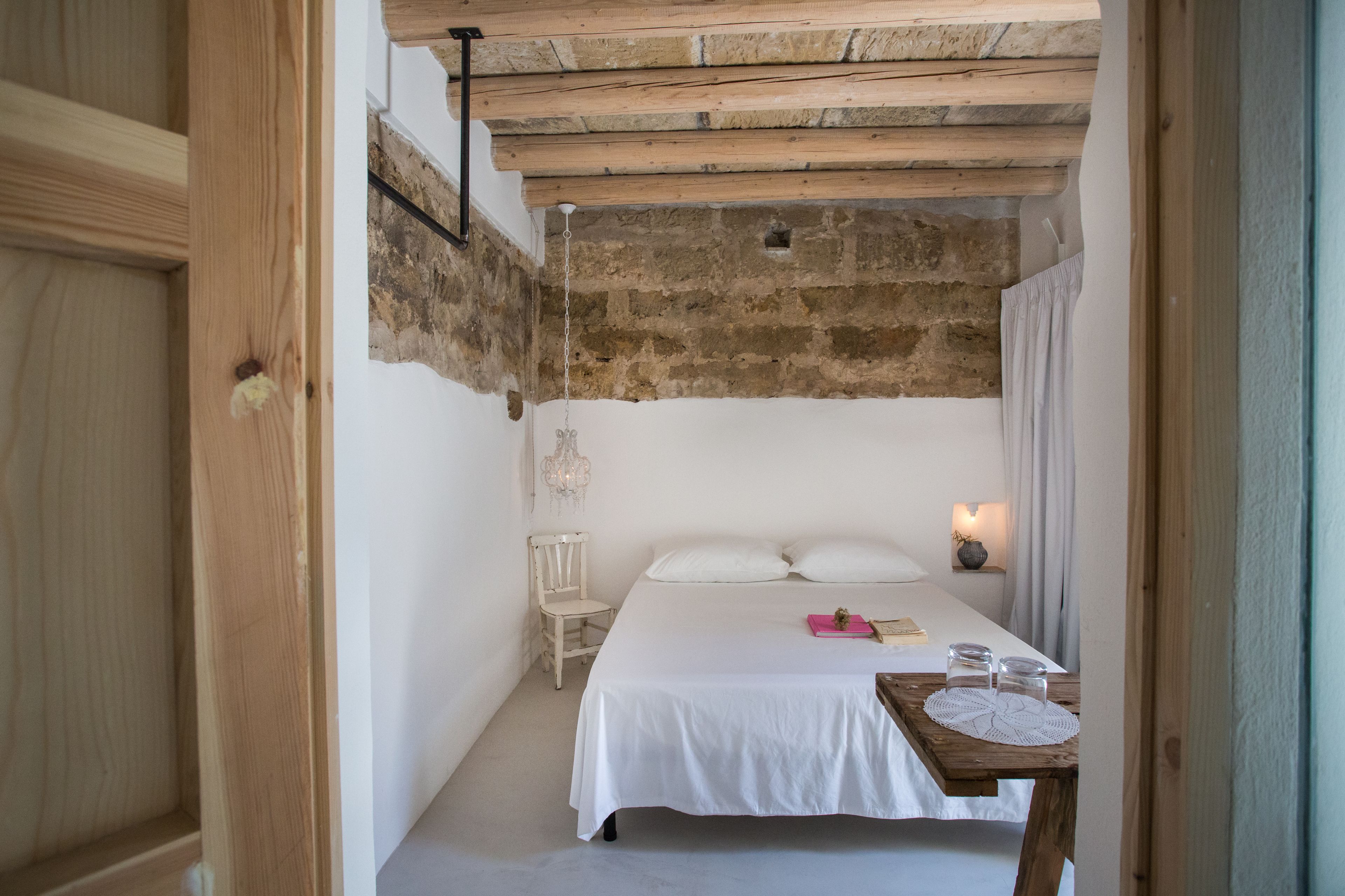 Une chambre avec un plafond en bois, un lit avec une literie blanche, une table de chevet avec une lampe et une chaise.