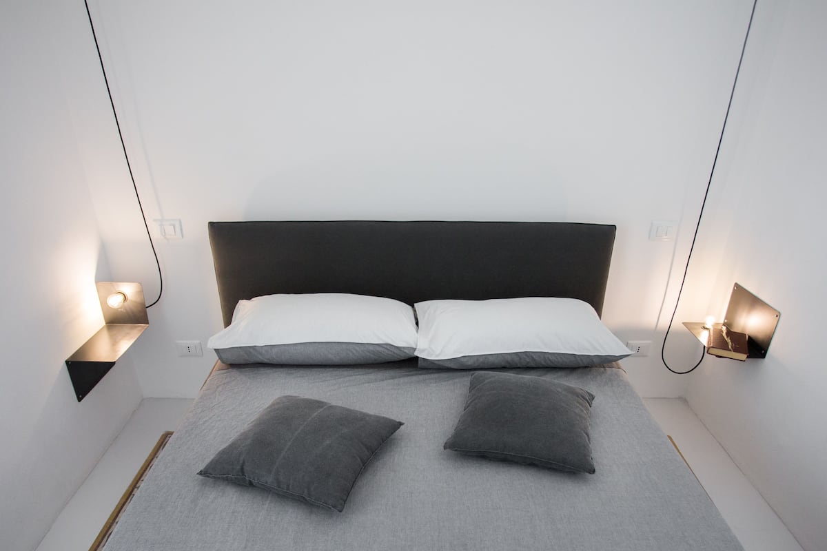 Un dormitorio moderno con una cama grande, dos mesitas de noche y luces de lectura fijadas en la pared.