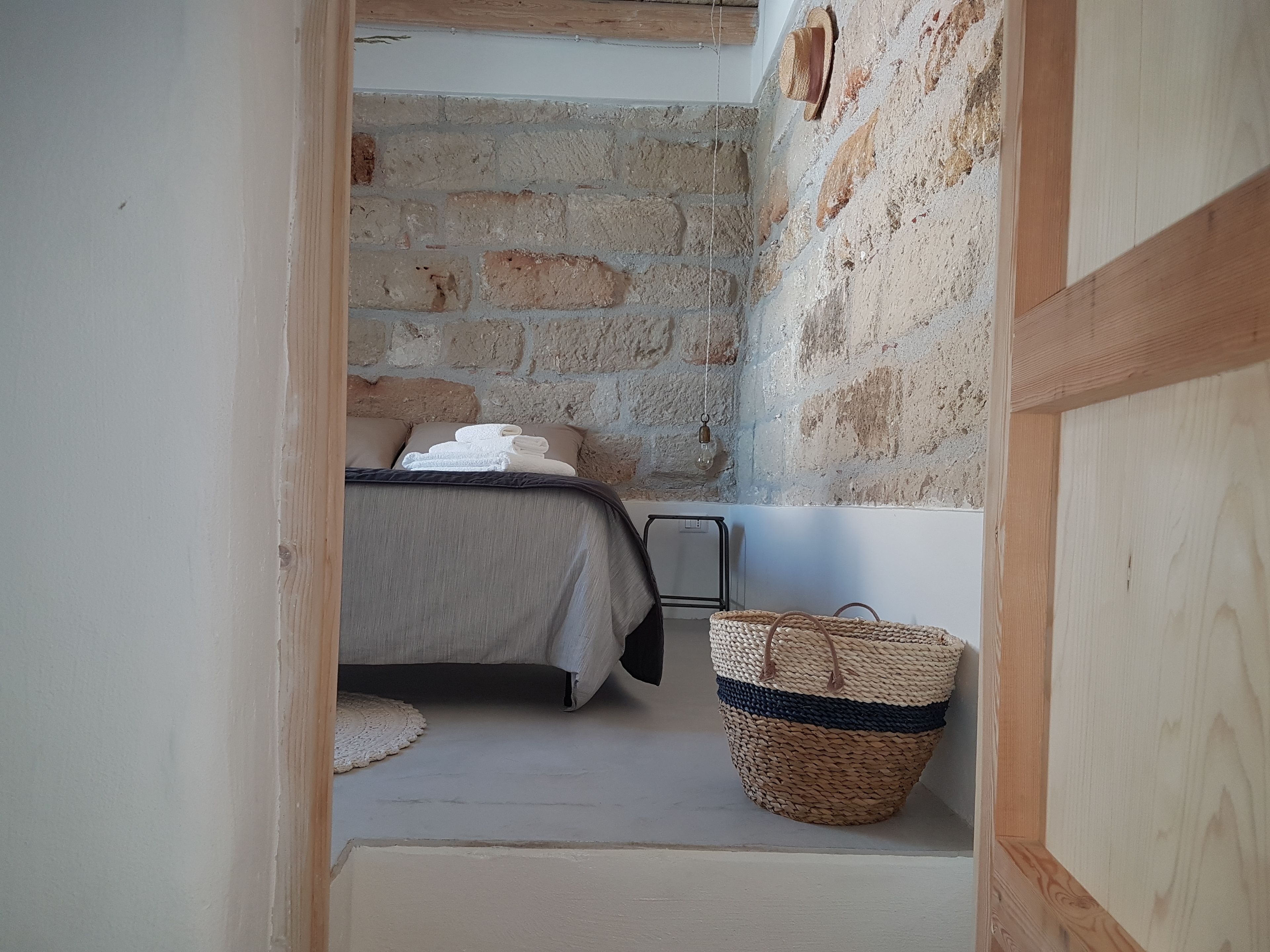 Una habitación estrecha con una cama, una cesta de mimbre y una pared de piedra.