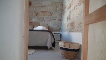 Una habitación estrecha con una cama, una cesta de mimbre y una pared de piedra.