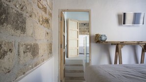 Un dormitorio con pared de piedra, una cama, una mesa de madera con un florero y un televisor en la pared.