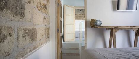 Un dormitorio con pared de piedra, una cama, una mesa de madera con un florero y un televisor en la pared.