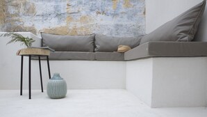 Un rincón con asientos que incluye un sofá gris, una mesita de madera con un florero y una pared con textura.